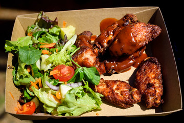 Barbecued chicken wings with vegetable salad in a cardboard box.
