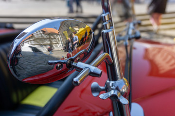 Focused chromed mirror of a red vintage car, deliberately blurred