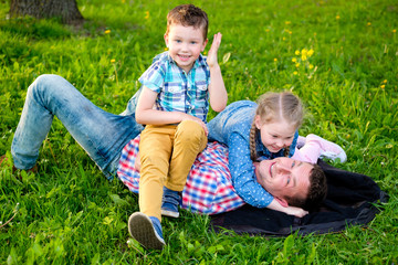 Naklejka na ściany i meble Happy and smile family in park, boy and girl have fun with Dad on the grass and looking at camera. Happy loving family concept