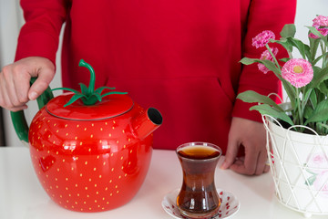 the woman put the tea in the glass with red teapot. 