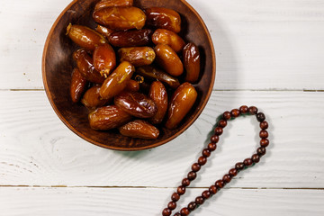 Dates fruit and rosary on white wooden table. Top view