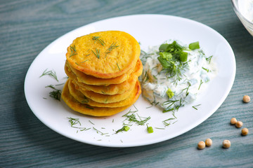 Peas flour pancakes and white yogurt sauce or salad with green vegetables. Pancakes made with peas flour and curcuma, and dip with soy yogurt and green onion and dill. Vegan dish.