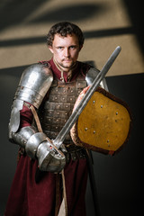 Medieval knight in armor holding sword and shield on the dark background