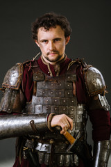 Medieval man knight in armor and weapon on dark background. Portrait of the knight