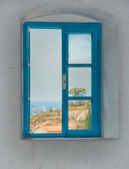 View of the city from the window of the building in the fortress of the old bar, Montenegro. Blue old window among white walls. Summer.