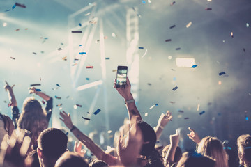cheering crowd with raised hands and falling confetti at concert - music festival