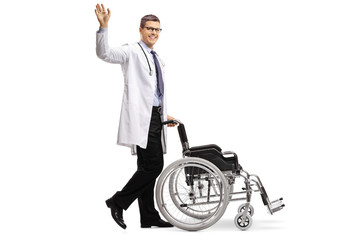 Young male doctor in a lab coat waving and pushing an empty wheelchair isolated