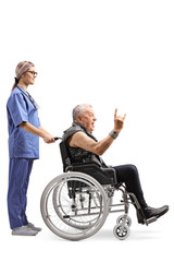 Obraz na płótnie Canvas Young nurse with a mature male patient making a rock and roll hand sign in wheelchair