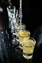 Bartender making yellow alcohol shots, black counter, black background.