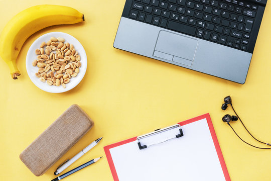 Yellow workplace with laptop, banana and peanuts. Snack at work. Top view. Flat lay