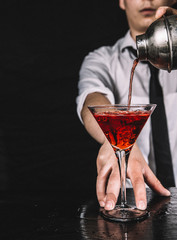 Bartender making a red martini cocktail. Barman pouring red liquor from a shaker, black background.
