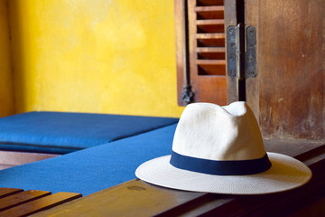 Straw hat on the window edge with yellow wall, wooden window frame and blue pillows in the background