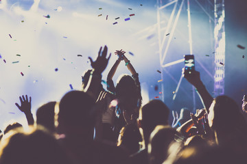 cheering crowd with raised hands and falling confetti at concert - music festival