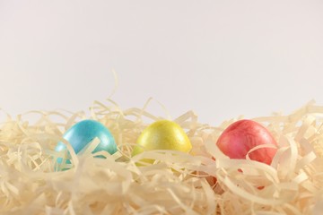 Three colored multi-colored eggs in a nest of chips along the underside of the frame.