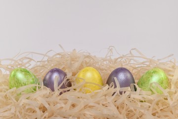 Five Easter colorful eggs in a nest of chips along the bottom of the frame. Front view from above. Minimum shadows in pastel tone.