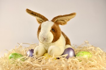 Plush rabbit paws on a yellow egg in a crispy nest with painted Easter eggs. Centrally located.