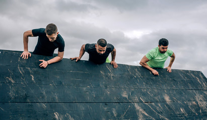 Group of participants in an obstacle course climbing an inverted wall
