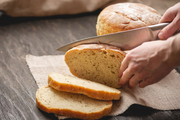 Hands cut with a knife homemade natural fresh bread with a Golden crust on wooden background. Baking bakery products