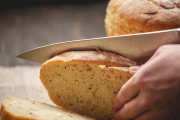 Hands cut with a knife homemade natural fresh bread with a Golden crust on wooden background. Baking bakery products