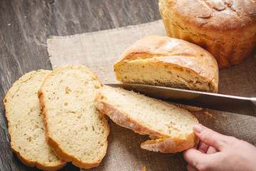 Hands cut with a knife homemade natural fresh bread with a Golden crust on wooden background. Baking bakery products