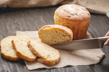 Hands cut with a knife homemade natural fresh bread with a Golden crust on wooden background. Baking bakery products