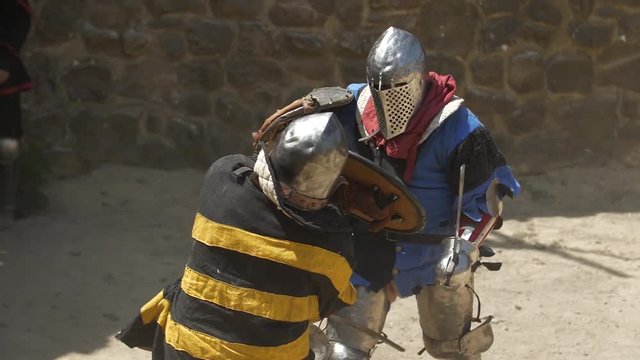 The brutal fight of two warriors in the sand arena Strikes with swords and shields Blue and yellow warriors