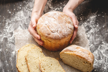 Hands holding homemade natural fresh bread with a Golden crust on an old wooden background. Baking bakery products