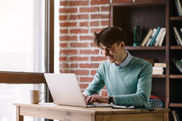 Fototapeta premium Young handsome student typing on his notebook his diploma. Student discussing on the phone universities's timetable. Education online. Work on freelance. Software development.