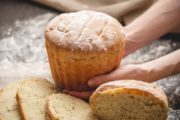 Hands holding homemade natural fresh bread with a Golden crust on an old wooden background. Baking bakery products