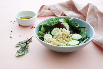 Beetroot salad with quinoa, cucumber, various lettuce leaves and onions on pastel pink background