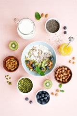 Homemade granola with milk. Ingredients granola oatmeal, nuts, chia seeds, pumpkin seeds, blueberries and kiwi. Pink background, empty space