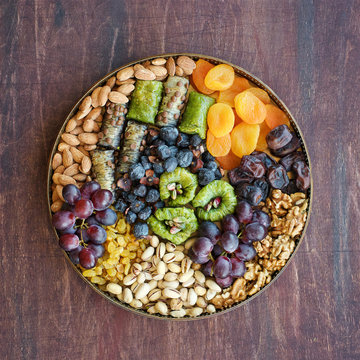Middle East sweets, dry fruits and nuts on a copper tray. Top view, wooden background