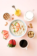 Oatmeal with honey, nuts and strawberries for breakfast. Light pink background. Flat lay
