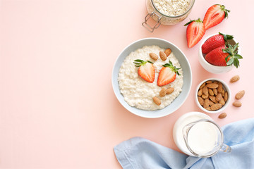 Oatmeal with honey, nuts and strawberries for breakfast. Light pink background. Flat lay