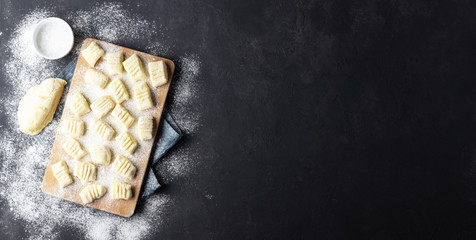 Raw uncooked homemade potato gnocchi with flour on cutting board. Top view. Dark background.