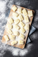 Raw uncooked homemade potato gnocchi with flour on cutting board. Top view. Dark background.
