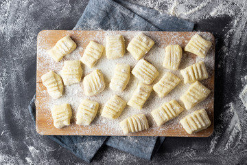 Raw uncooked homemade potato gnocchi with flour on cutting board. Top view. Dark background.