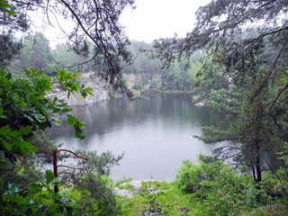 Abandoned flooded quarry in the forest. Lake in the forest. Geological outcrops