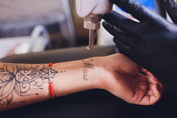 Cosmetologist with patient and professional tattoo removal laser in salon.