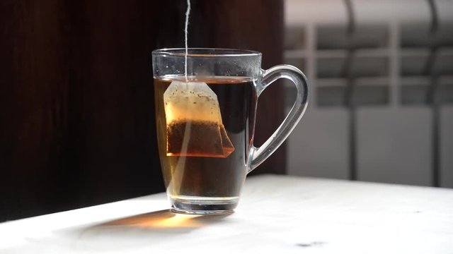 brew a bag of black tea. transparent cup with hot water and teabag on black background, add lemon