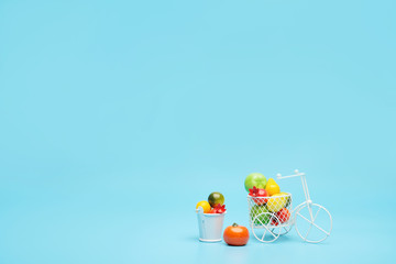 White wire bicycle with a basket filled with mini fruit. Near the bucket with vegetables and fruits. Blue background. Concept of harvesting and delivering fruits and vegetables.