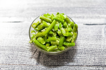 Frozen beans. Glass bowl with frozen green beans on beautiful wooden background