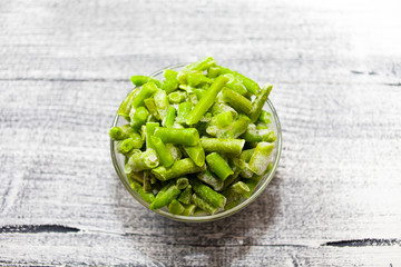 Frozen beans. Glass bowl with frozen green beans on beautiful wooden background