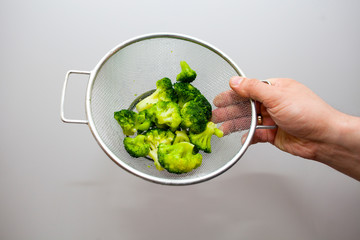 Frozen broccoli in a colander, on a wooden background. Healthy diet.