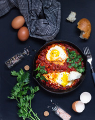 Fried eggs in tomato sauce with parsley and bread in a cast-iron pan. Shakshuka, typical Israel food. Breakfast or lunch. 