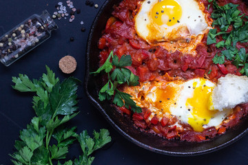 Fried eggs in tomato sauce with parsley and bread in a cast-iron pan. Shakshuka, typical Israel food. Breakfast or lunch. 