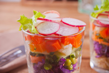 Healthy fresh salad in glassful with red cabbage, tomato, quinoa, green salad and radish on the wooden table
