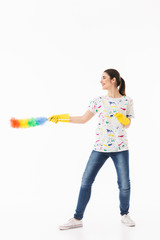 Photo of positive woman 20s wearing yellow rubber gloves holding colorful duster while cleaning room