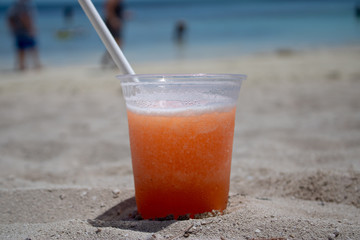Close up of an orange & mango tropical cocktail overlooking a beautiful blurred beach setting background.