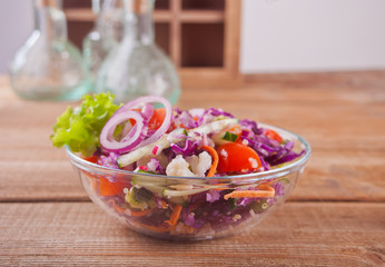 Healthy fresh salad in bowl with red cabbage, tomato, quinoa, green salad and radish on the wooden table
